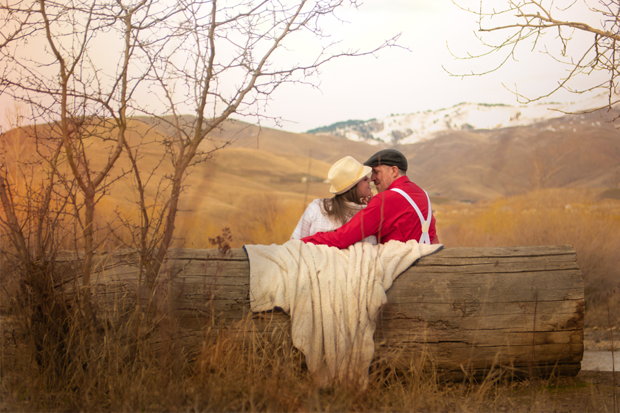 Couple sitting on a log bench surrounded by fall colors nearly kissing.
