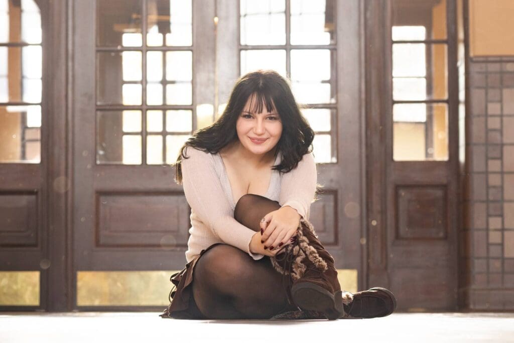 High school senior sitting on the floor inside the Boise Train Depot with wood doors in the background.