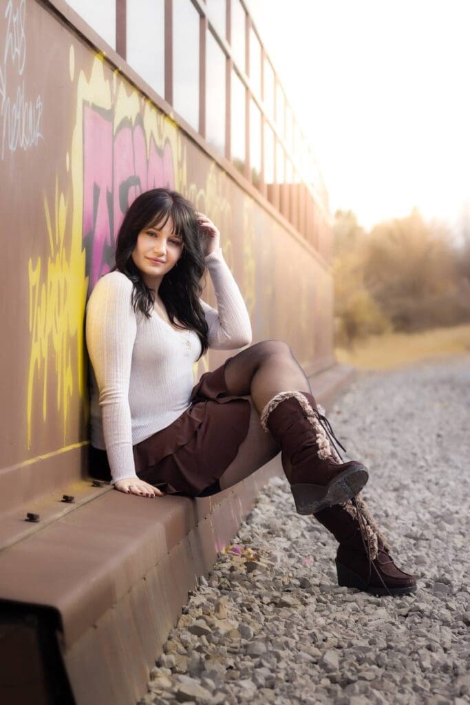 High school senior sits on the edge of a metal wall covered in graffiti.